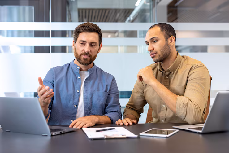 two-men-discuss-business-strategy-working-laptops-modern-office-table